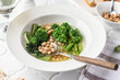 Vegetarian minestrone soup with green vegetables and beans served in white plate and bread on white tile table close up