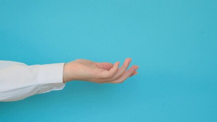 Wall Mural - A hand in a white shirt holds something on a blue background. 4k footage