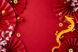 Theme for Chinese New Year: honoring traditions. Top view flat lay of gold dragon, red paper fans, traditional coins, sakura bloom on red background with advert area