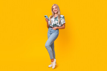 Sticker - Full size photo of optimistic girl dressed print shirt stylish jeans holding smartphone arm in pocket isolated on yellow color background