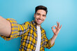 © deagreez - Photo of positive handsome man dressed yellow plaid shirt showing okey gesture tacking selfie isolated blue color background