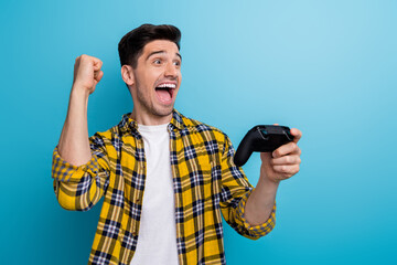 Poster - Photo of excited lucky man dressed yellow plaid shirt winning playstation video game empty space isolated blue color background