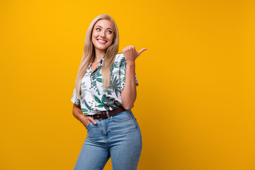 Poster - Portrait of cute girl with long hair wear flower print blouse look indicating at offer empty space isolated on yellow color background