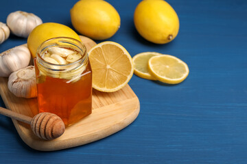 Wall Mural - Honey with garlic in glass jar, lemons and dipper on blue wooden table. Space for text