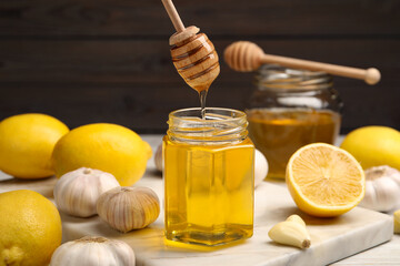 Wall Mural - Honey dripping from dipper into jar, garlic and lemons on table