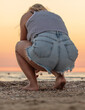 A woman in denim shorts squats at sunset