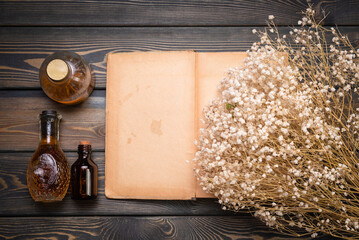 Wall Mural - Remedy elixir recipe template. Herbal medicine concept background. Dry gypsophila flowers, remedy bottle and blank paper book page on the wooden table flat lay background with copy space.