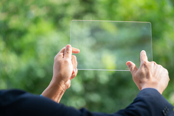 Wall Mural - Hand holding and showing transparent tablet device. Business, natural green bokeh background,technology concept,alternative energy,conservative clean energy .