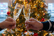 © barmalini - New year or christmas dinner, two man hands with glasses of champagne cava or prosecco wine crystal glasses with christmas tree and garland lights on background