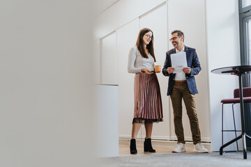 A group of business professionals walking and discussing project details in a modern office hallway.