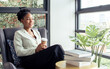 © Ann Rodchua - Portrait African smart business female entrepreneur, manager wearing formal green suit, smiling with confidence, holding cup of coffee, sitting on sofa beside window in morning at modern office.