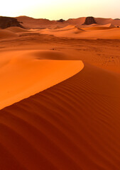  Sahara desert, orange dunes. Holidays and travel in Algeria, morning light over the desert. Rocks in the background. Fine lines of sand dunes.