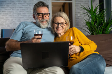 Poster - Excited husband and wife watching funny content on laptop with wine in evening at home