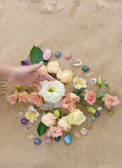 Wall Mural - Hand with gemstones and flowers for Crystal Ritual on sand background. Esoteric spiritual wiccan practice for relaation, harmony, life balance. spa concept. Flower Mandala with crystals. top view