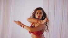 Beautiful Girl Dances Oriental Belly Dance. Sexy Woman In Red Lingerie Is Dancing A Seductive Dance In A White Studio. Beautiful Stomach And Breasts.	
