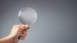  a person's hand holding a magnifying glass over a gray background with only one hand holding a magnifying glass.