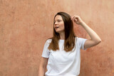 Fototapeta Tematy - Portrait of a beautiful young woman with long brown hair in a white T-shirt on a concrete wall background