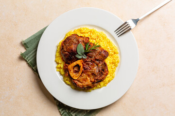 Canvas Print - Top view of plate with Italian dish Ossobuco, braised beef meat with bone served with saffron risotto alla milanese, specialty of Lombard cuisine. Beige background.