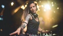 Attractive young female DJ with tattoos and long hair playing music and dancing in a club, focus on mixing pult