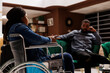 Young African American woman tourist with disability sitting in hotel lobby with husband, arriving at wheelchair accessible hotel. Able-bodied man traveling with disabled girlfriend