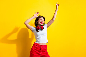 Wall Mural - Portrait of relaxed pretty girl wear white t-shirt dancing in red headphones hold hands up enjoy party isolated on yellow color background