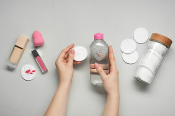 Wall Mural - Woman with makeup remover, cotton pads, foundation, lip gloss and sponge on light grey background, top view