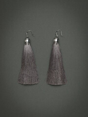 Women's silver earrings with gray threads on a gray background.