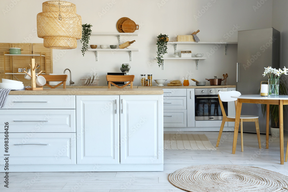 Interior of light kitchen with stylish fridge, counters, shelves, table and chairs