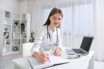 Wall Mural - Beautiful doctor writing at table in clinic