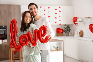 Wall Mural - Happy young couple with word LOVE made of balloons in kitchen on Valentine's Day