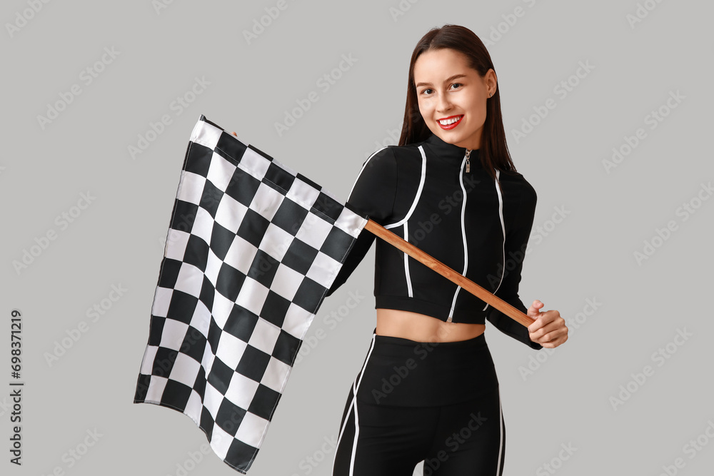 Beautiful young woman with racing flag on grey background