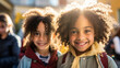 Two cheerful siblings with curly hair share a radiant smile, highlighted by the golden sunlight behind them.