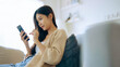 © Monster Ztudio - Happy young asian woman relax on comfortable couch at home texting messaging on smartphone, smiling girl use cellphone, chatting online message, shopping online from home