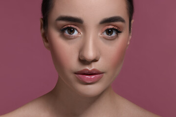 Wall Mural - Portrait of beautiful young woman with perfect makeup on dark pink background, closeup