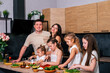 © dvulikaia - Young parents watch as their four daughters prepare vegetarian salad in the kitchen. Large happy family at home.