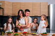 © dvulikaia - Young parents cook vegetarian salad at the kitchen with their daughters.