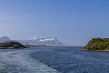 View of the commercial and tourist port in the city of Bodo from the ferry on Lofoten Island on a sunny summer day under a blue sky, a boat with a sail on the water in the sea