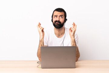 Wall Mural - Telemarketer caucasian man working with a headset and with laptop with fingers crossing and wishing the best.