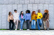 © Koldo_Studio - Diverse group of seven young friends enjoying time together by a gray wall, showcasing racial diversity and joyful interaction.