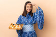 Woman wearing kimono and holding sushi over isolated background saluting with hand with happy expression
