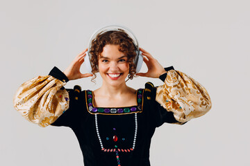 Wall Mural - Young adult woman with headphones on her head and dressed in a medieval dress listens music isolated white background