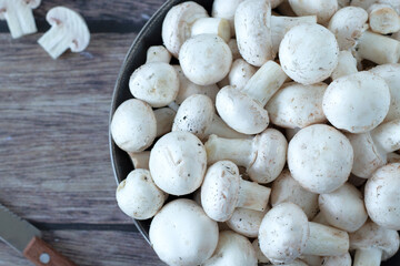 Wall Mural - White button champignon mushrooms (agaricus bisporus) in a bowl with knife on wooden table. Top view, close-up.