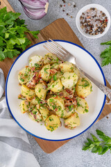 Wall Mural - Warm potato salad with bacon, onion, fresh herbs and vinegar dressing in a bowl on a gray concrete background. German Kartoffelsalat.