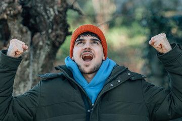 young man bundled up in winter outdoors celebrating excited with joy