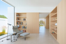 Modern Living Space With Wooden Bookshelf, Designer Chair, And Ample Sunlight Entering Through Large Windows