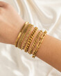 Girl wearing set of gold chain bracelets on wrist with silky fabric background