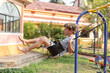 © Татьяна Волкова - Cute boy ingray T-shirt, shorts is swinging on swing on playground on summer day. Summer holidays.