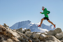 Runner In A Green Jacket Leaping Between Rocks In High Altitude