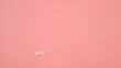 The surface of water on a pink background. Bubbles are visible on the water.