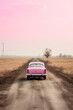 © ADDICTIVE STOCK - Generative AI illustration of pink vintage car on a dirt road amidst barren fields under a pastel sky